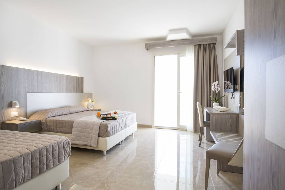 A modern hotel room with two beds, a desk, and a television.
