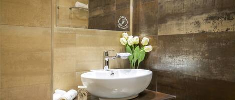 A bathroom with a large white sink, a mirror, and a vase with white flowers.