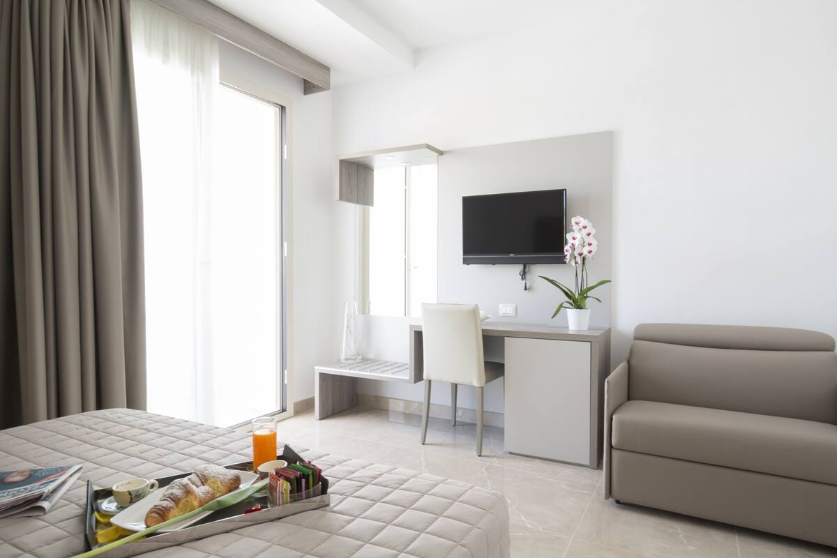 A modern hotel room with a bed, a desk, a TV, and a sofa.
