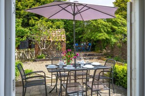 A patio with a table set for dining, surrounded by chairs, and an umbrella providing shade. - Jasmine Cottage, South Creake, Norfolk (South Creake)