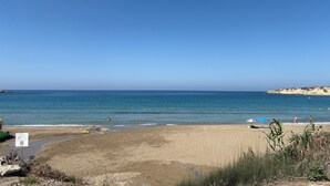 Una spiaggia con cielo sereno, acqua calma e alcune persone che nuotano.
