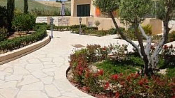 Un edificio moderno con facciata beige, un balcone e un giardino curato con fiori rossi e un vialetto.