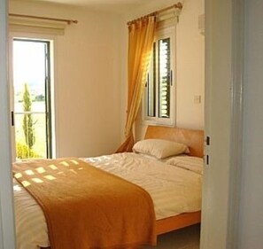 Une chambre à coucher avec un lit, une fenêtre avec des rideaux et une vue sur la verdure à l’extérieur.
