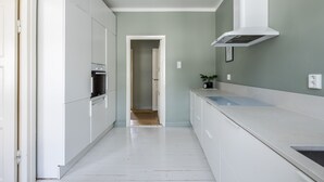 A narrow kitchen with white cabinets, a microwave, and a white range hood. - Scandinavian Apartments Fredrikinkatu (Helsinki)