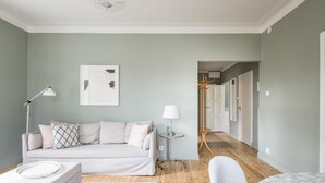 A modern living room with a light green wall, a white sofa, a small side table with a lamp, and a wooden floor. - Scandinavian Apartments Fredrikinkatu (Helsinki)