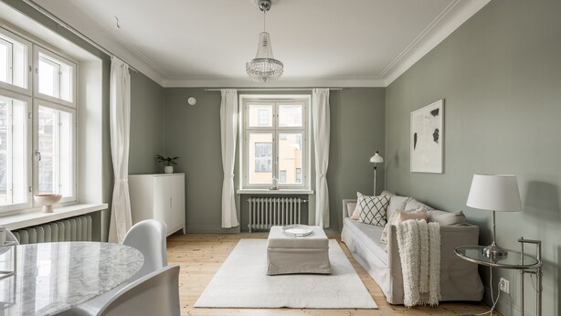 A modern living room with a dining area, a sofa, a radiator, and a chandelier. - Scandinavian Apartments Fredrikinkatu (Helsinki)