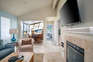 A living room with a fireplace, a television mounted on the wall, and a dining area with a table and chairs.