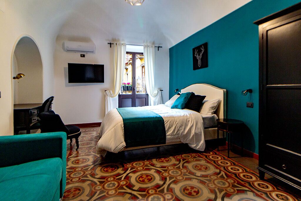 Habitación de hotel con cama, televisión, armario y alfombra estampada.