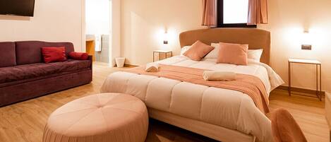 A modern bedroom with a large bed, a sofa, and a round ottoman.