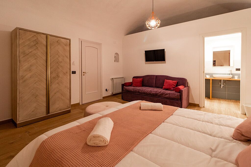A bedroom with a bed, a wardrobe, a sofa, and a bathroom visible through an open door.