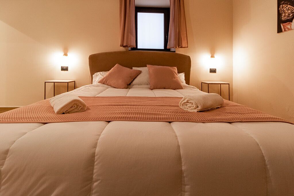 Un lit bien fait, avec une couette et des oreillers de couleur beige, deux tables de chevet avec des lampes et une fenêtre avec des rideaux.