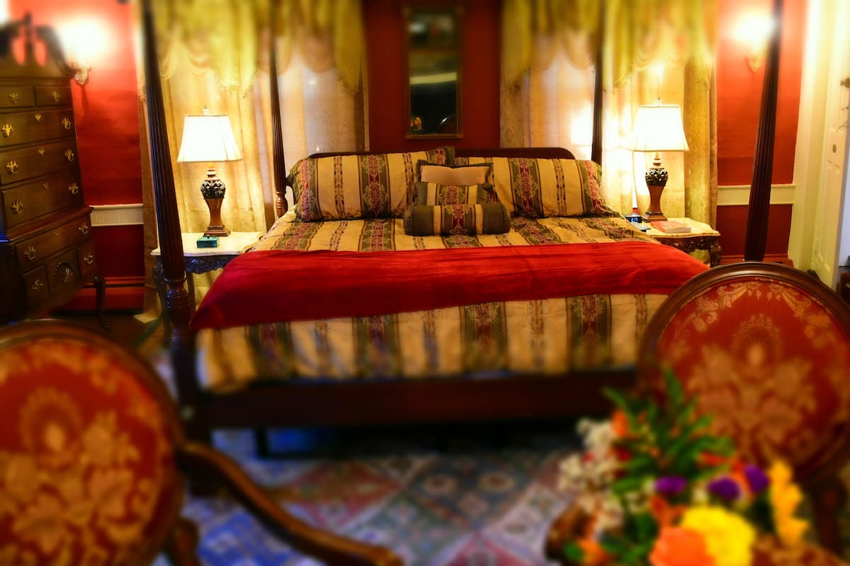 A hotel room with a large bed, two bedside tables with lamps, a dresser, and a floral arrangement.