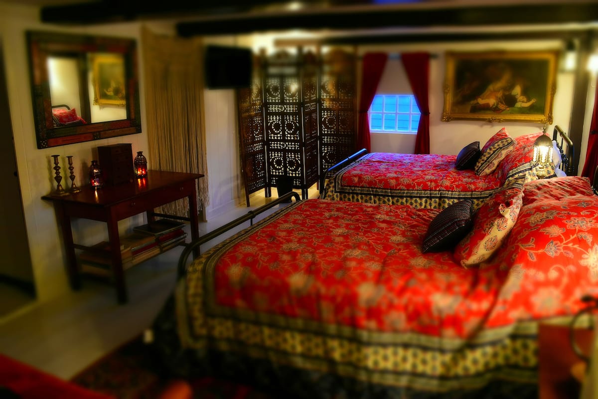 A bedroom with two beds, a desk, and a mirror.