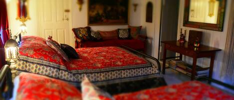 A bedroom with a large bed, a wooden nightstand, a desk, and a painting on the wall.
