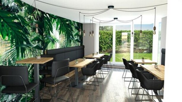 Un comedor moderno con un mural tropical, mesas de madera y sillas negras.
