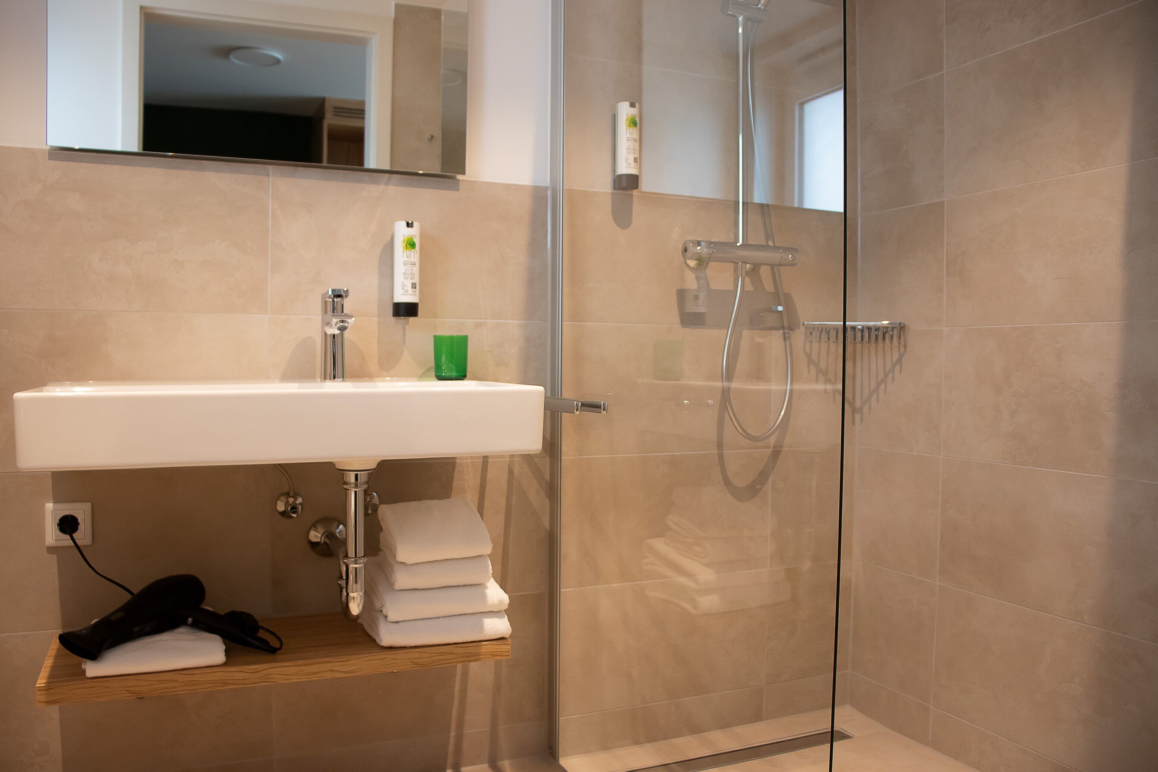 A modern bathroom with a glass-enclosed shower, a white sink, and a wooden shelf with towels.