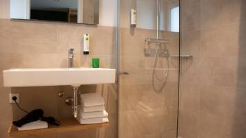 A modern bathroom with a glass-enclosed shower, a white sink, and a wooden shelf with towels.