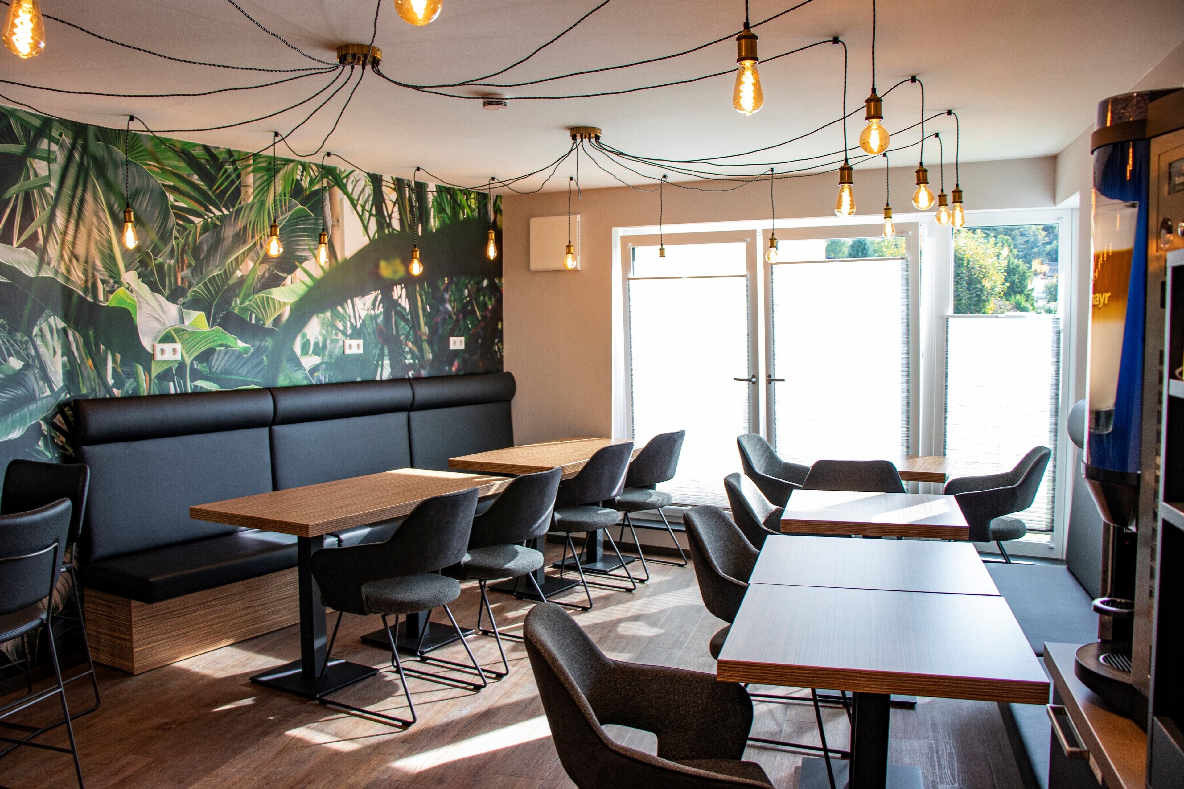 A modern cafe with a black leather booth, wooden tables, and chairs.