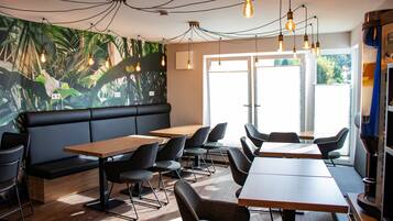 A modern cafe with a black leather booth, wooden tables, and chairs.