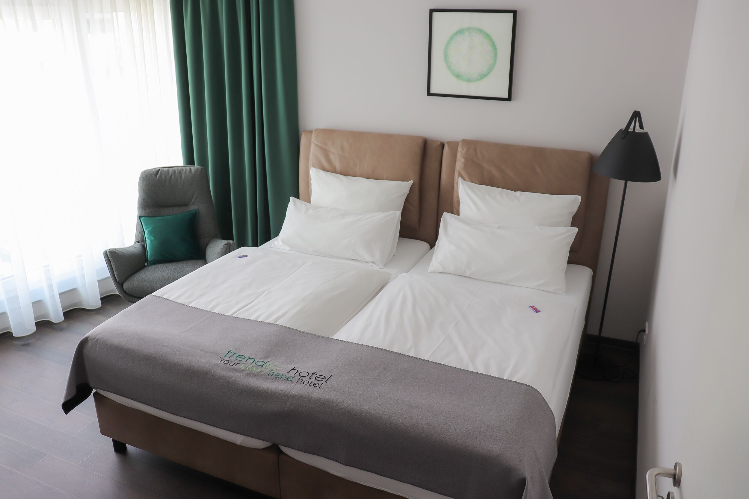 Une chambre d’hôtel avec un lit, une chaise, une lampe et un tableau encadré au mur.