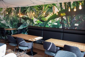 A restaurant with a modern interior, featuring a long wooden table, several grey upholstered chairs, and a black cushioned bench. - trendic hotel (Marktoberdorf)