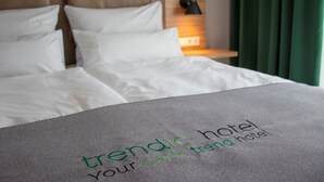 Una cama bien hecha con una manta gris y un cojín con la inscripción 'trendic hotel your basic trend hotel'.