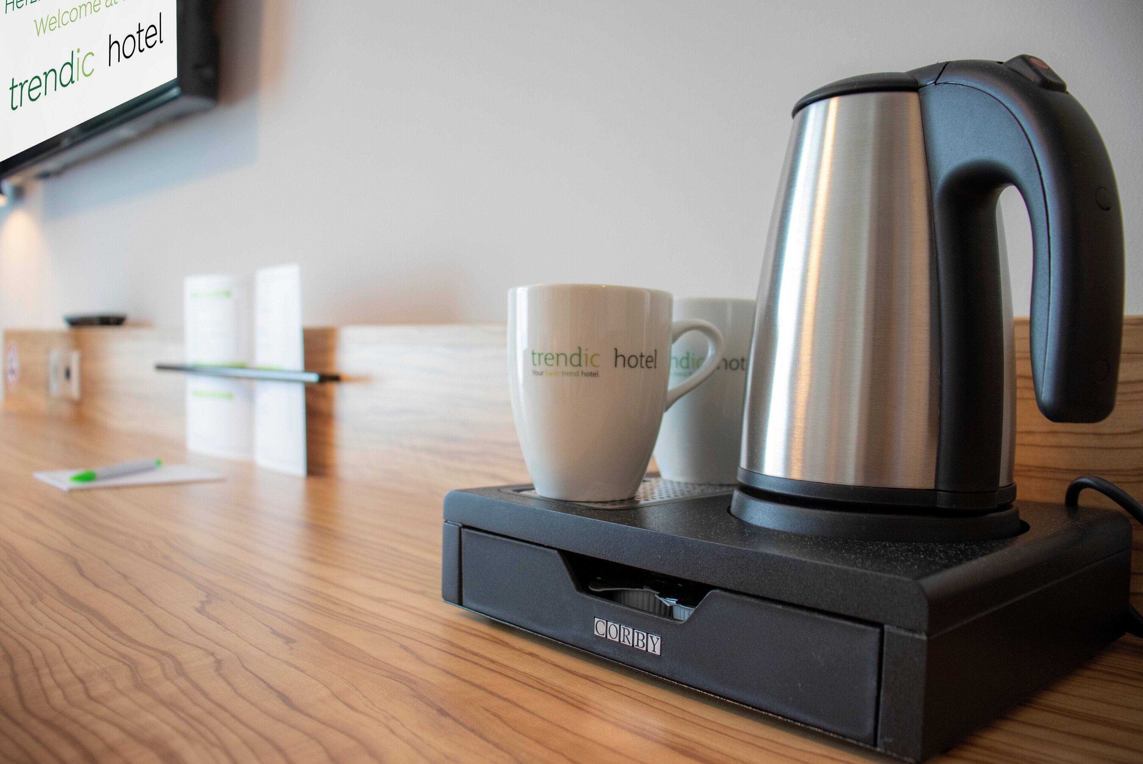 Une machine à café est posée sur une table en bois, à côté de deux tasses blanches et d’une boîte de mouchoirs.