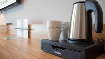 Une machine à café est posée sur une table en bois, à côté de deux tasses blanches et d’une boîte de mouchoirs.