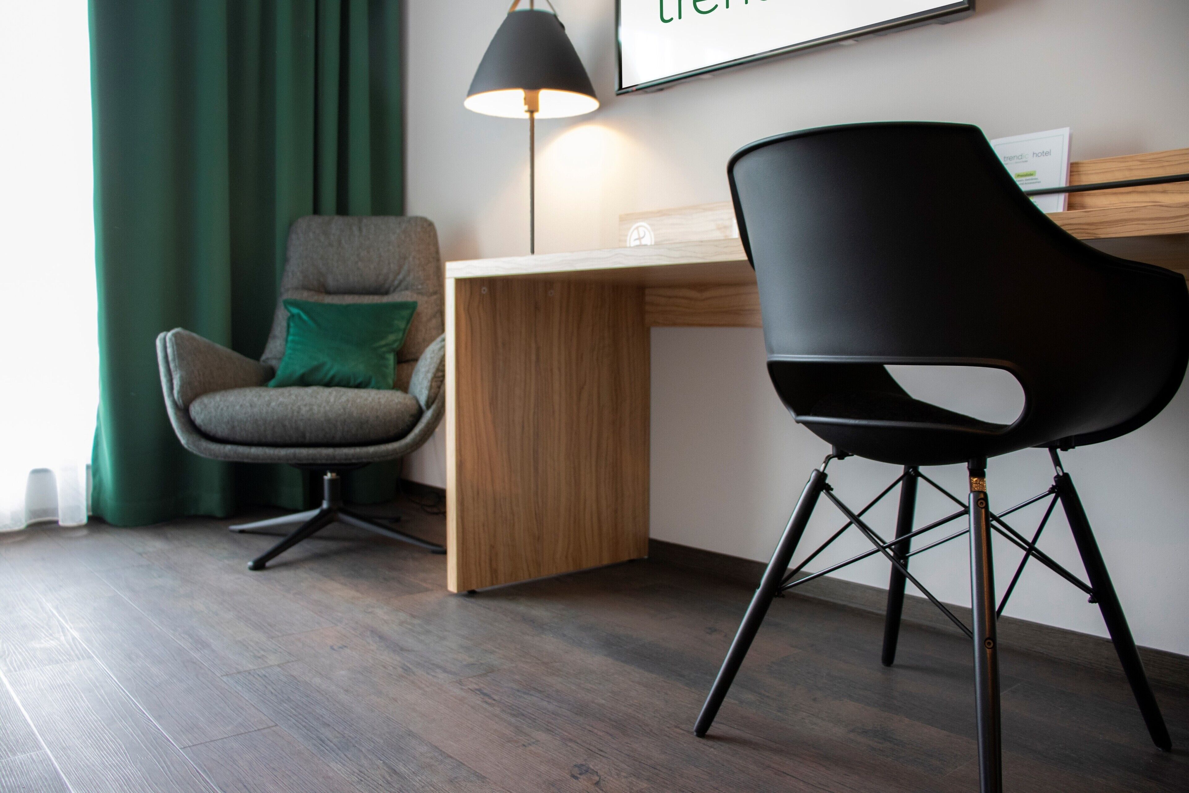 A modern room with a wooden desk, two chairs, a lamp, and a framed sign on the wall.