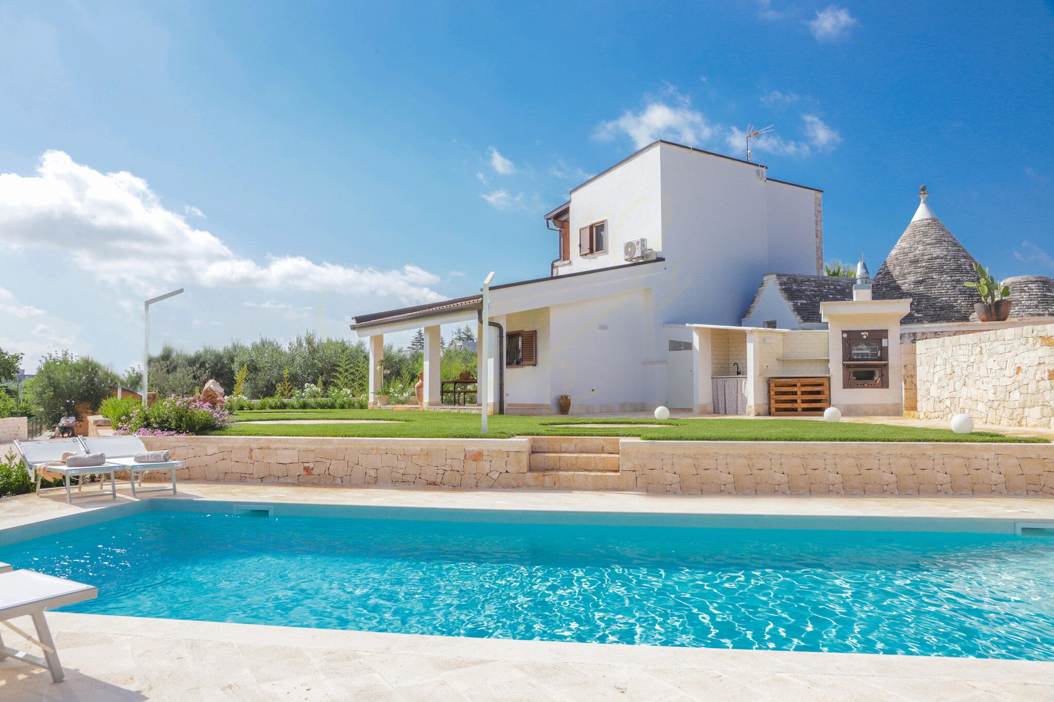 A modern house with a swimming pool, stone walls, and a well-maintained garden.