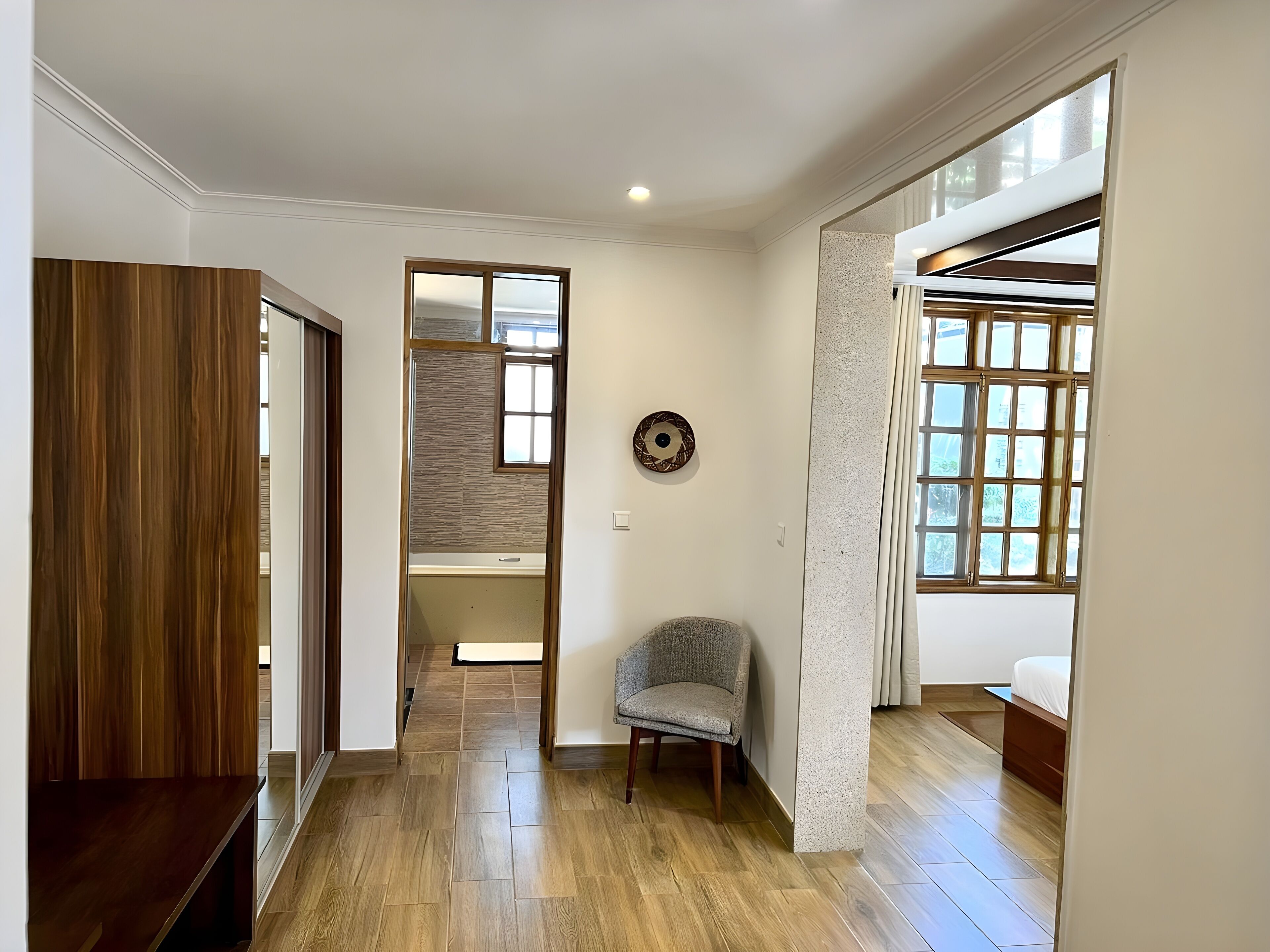 A spacious room with a wooden floor, a chair, a bed, and a large window.