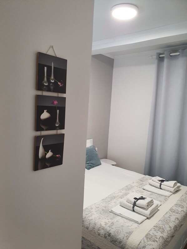 A neatly arranged bedroom with a bed, a bedside table, and a wall-mounted shelf with vases. - Happy Apartments (Mostar)