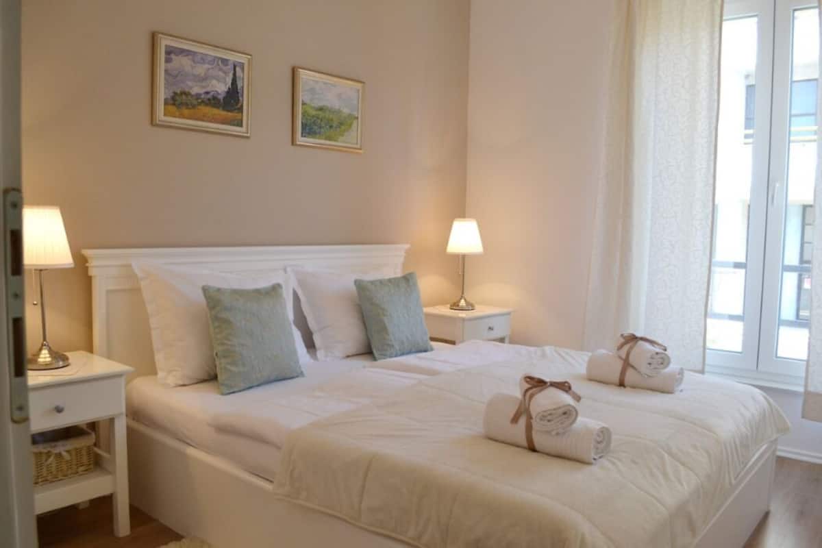 Un lit bien fait, avec du linge de lit blanc et des oreillers, deux lampes de chevet et deux tableaux encadrés accrochés au mur.