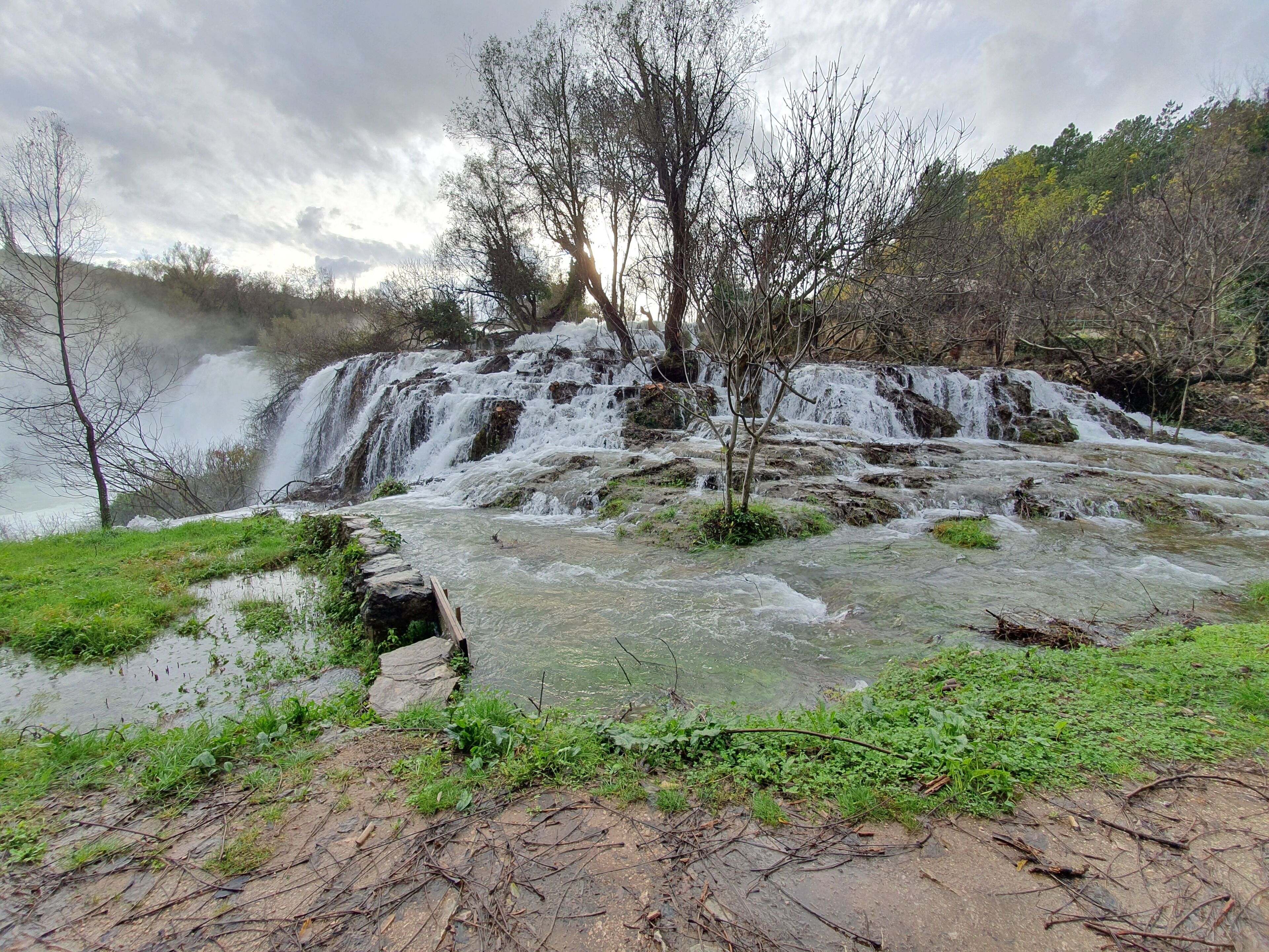 A natural landscape with a waterfall, rocky terrain, and sparse vegetation.