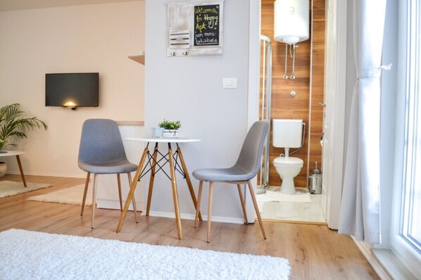 A modern living room with a white sofa, two grey chairs, a small table, and a TV mounted on the wall. - Happy Apartments (Mostar)