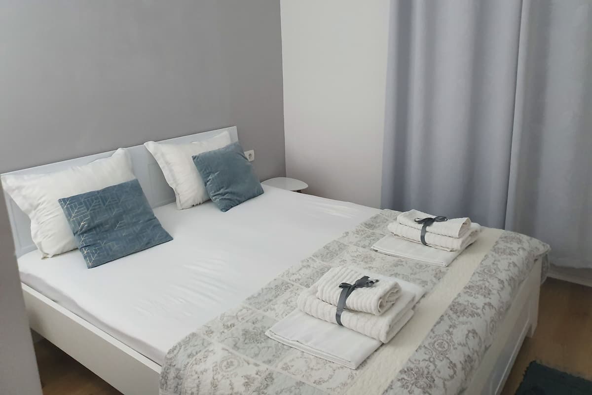 Un lit bien fait, avec une couvre-lit à motifs, deux oreillers et des serviettes pliées sur une table de chevet blanche.