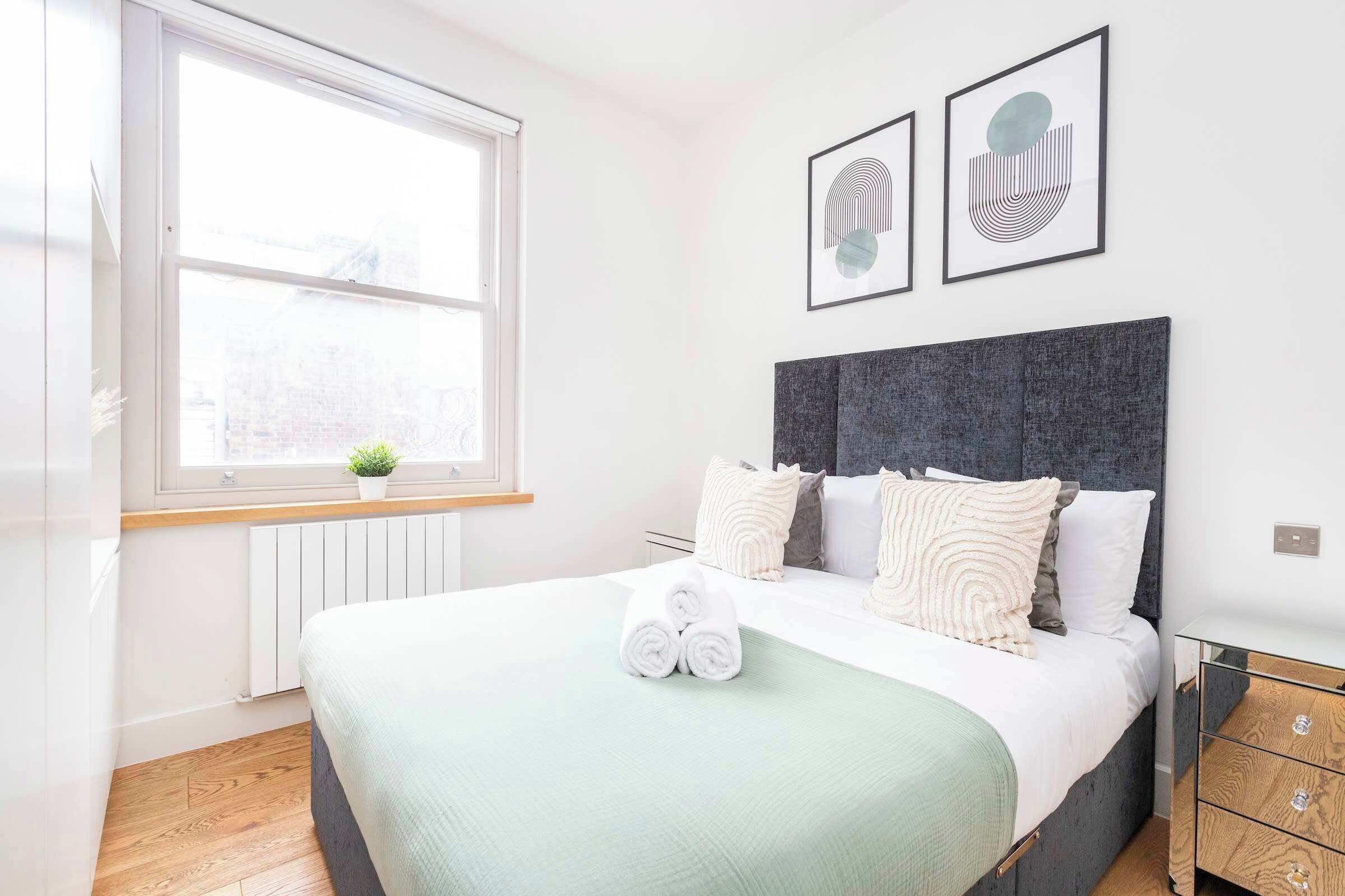 A modern bedroom with a large bed, a window, and two framed artworks on the wall.