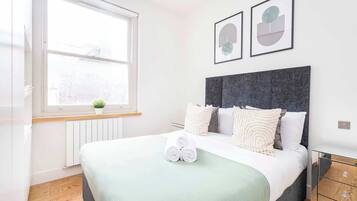 A modern bedroom with a large bed, a window, and two framed artworks on the wall.