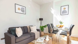 A modern living room with a grey sofa, a glass coffee table, and a dining area with a glass table and chairs. - Fitzrovia Lovely 1BR Flat (London)
