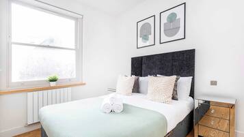 A modern bedroom with a large bed, a bedside table, a radiator, and a window with a view.