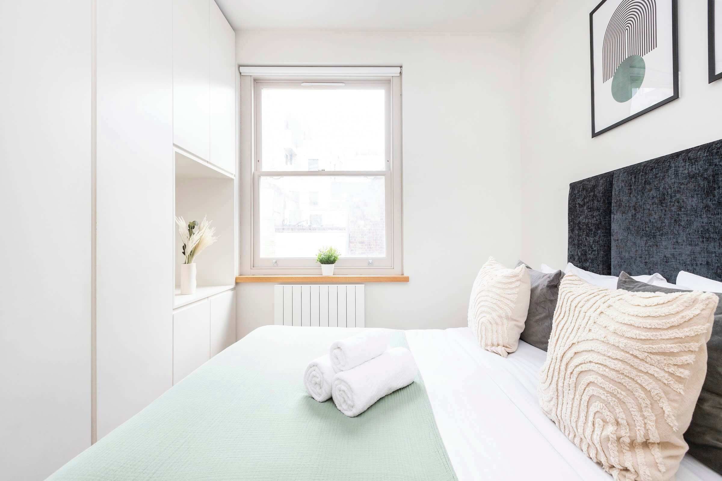 A neatly arranged bedroom with a bed, pillows, a window, and a small plant on the windowsill.