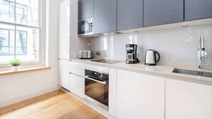 A modern kitchen with white cabinets, a stainless steel microwave, a toaster, a coffee maker, and an oven. - Fitzrovia Lovely 1BR Flat (London)