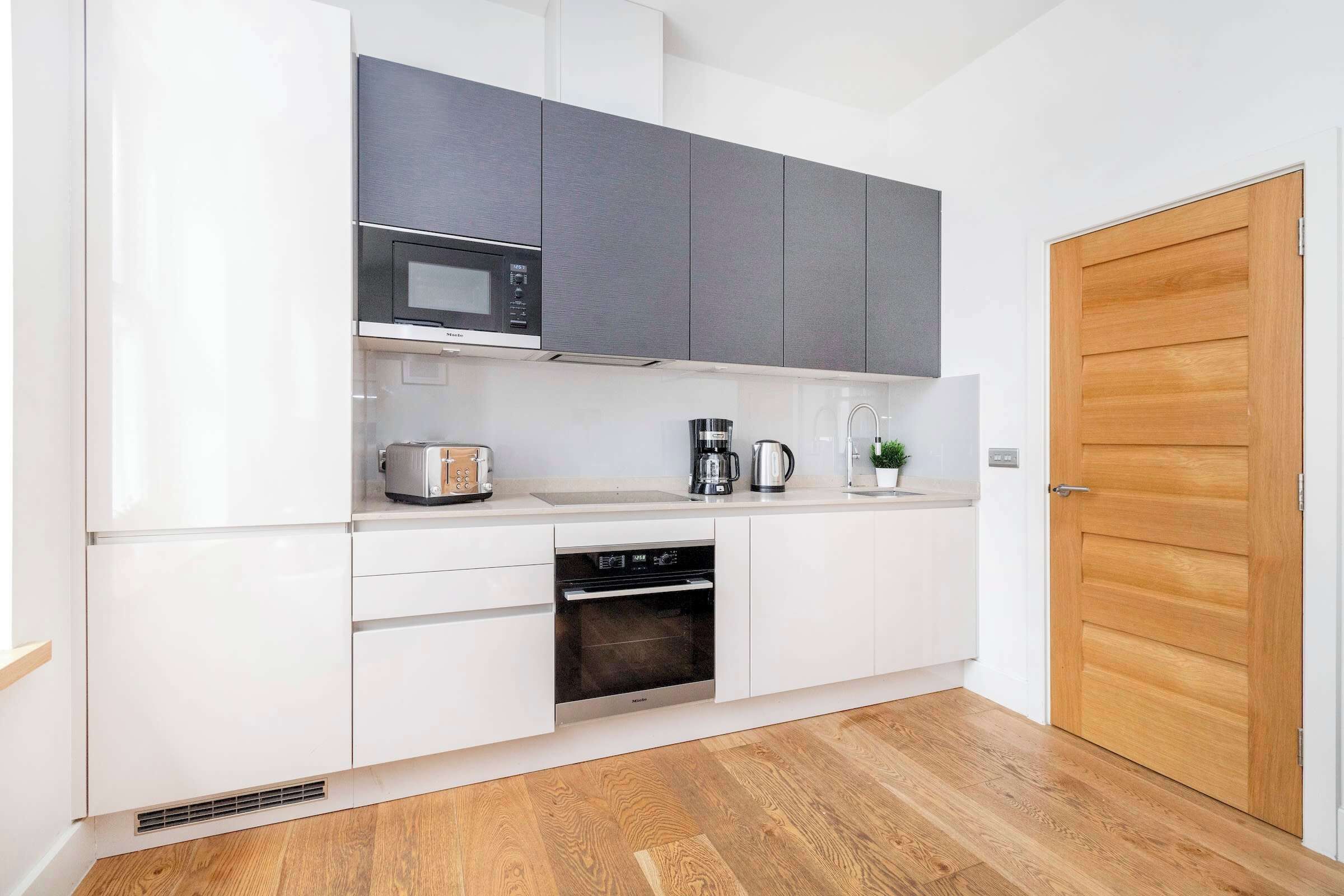 A modern kitchen with white cabinets, a microwave, a coffee maker, and an oven.