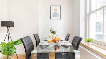A modern dining area with a glass table, black leather chairs, and a fruit bowl.