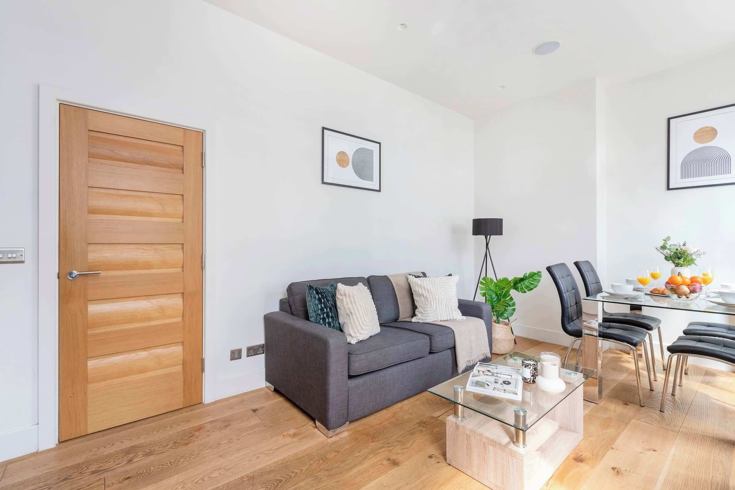 A modern living room with a grey sofa, a glass coffee table, and a dining area with a glass table and chairs.