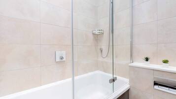 Een moderne badkamer met een douchecabine van glas, een witte badkuip en een klein plankje met planten.