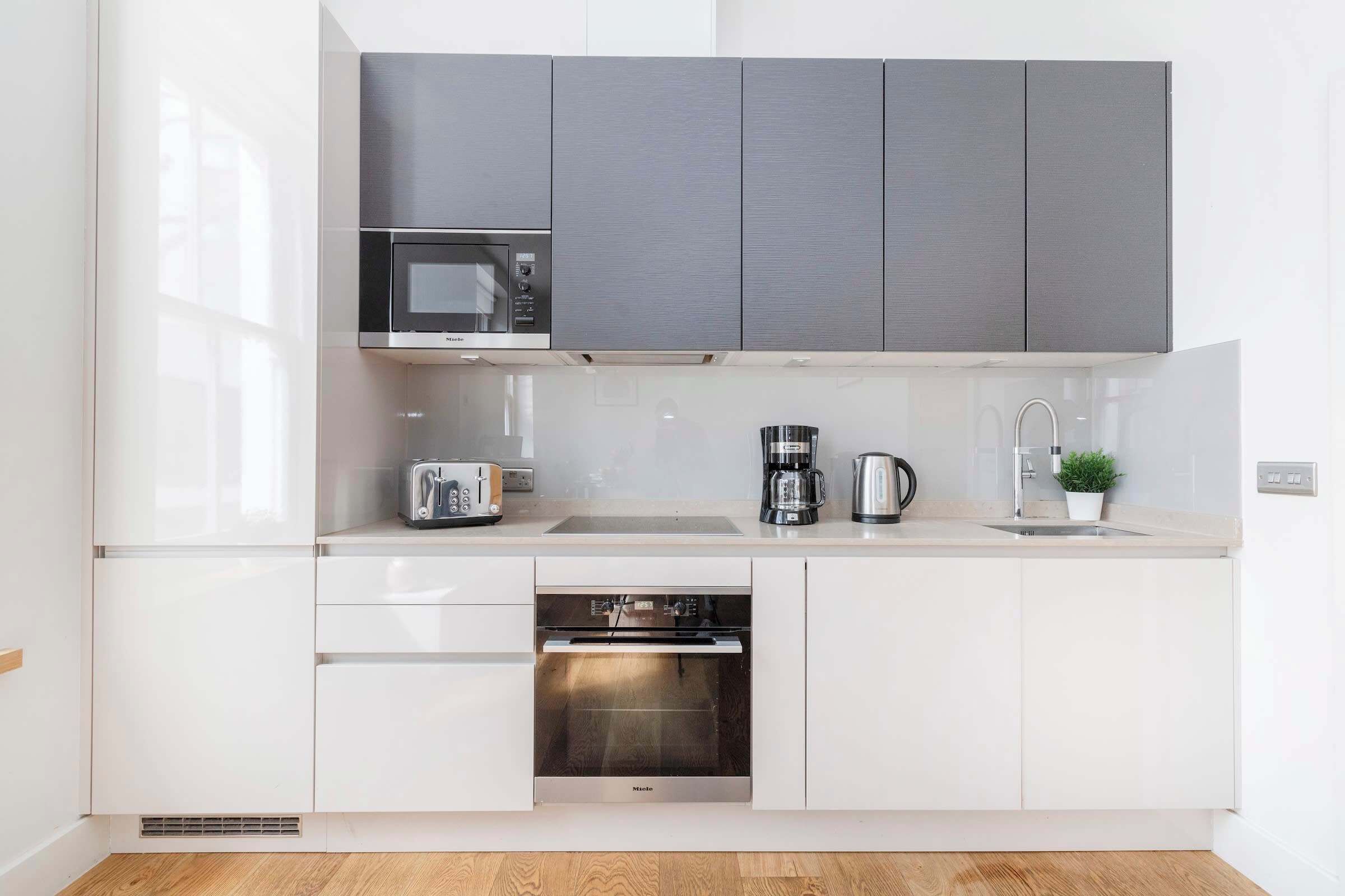 A modern kitchen with white cabinetry, a built-in microwave, a toaster, a coffee maker, and an oven.