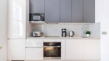 A modern kitchen with white cabinetry, a built-in microwave, a toaster, a coffee maker, and an oven.