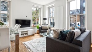 Una sala de estar moderna con una mesa de centro de vidrio, un sofá gris, una mesa de comedor blanca y un televisor de pantalla plana.