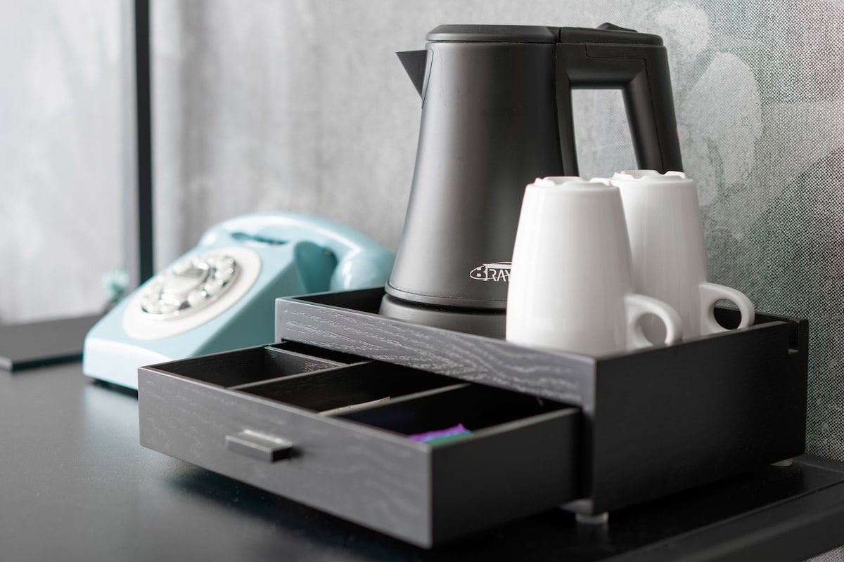 Organizador de gaveta com cafeteira, xícaras, um telefone antigo e uma chaleira preta sobre uma mesa.